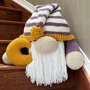 Photo of 18" crocheted gnome. With purple and white striped hat and a moon shaped pillow in his hands