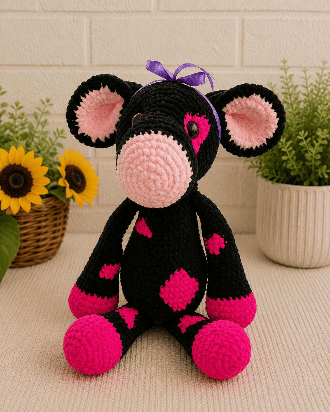 Handmade crochet cow plush in black and pink yarn sitting on a neutral textured surface.