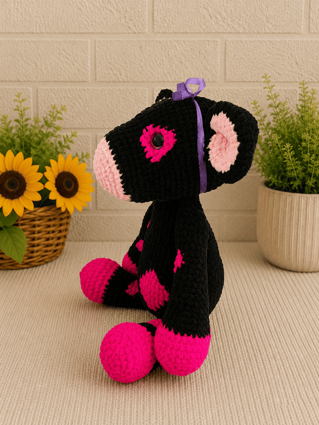 Side profile of handmade crochet black and pink cow plush with purple ribbon.
