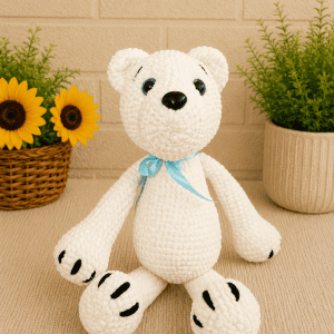 Handmade crochet polar bear sitting with blue ribbon.