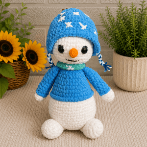 Handmade crochet winter snowman plush wearing a blue sweater, scarf and star-print hat.